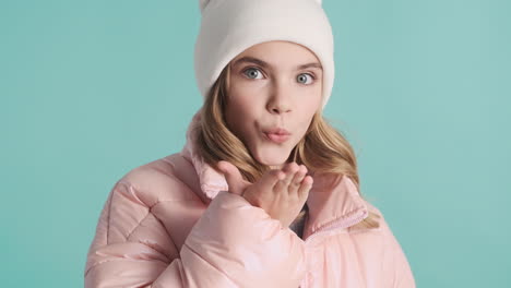 teenage caucasian girl with winter clothes sending kisses to the camera.