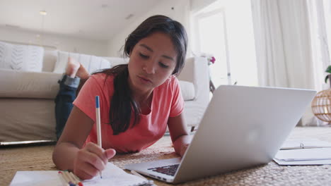 Teenage-girl-lying-on-the-floor-doing-her-homework-using-a-laptop-computer,-low-angle,-close-up