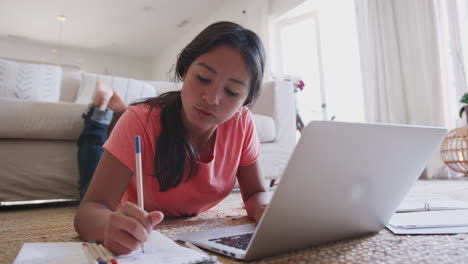 una adolescente tendida en el suelo haciendo su tarea usando una computadora portátil, ángulo bajo, primer plano