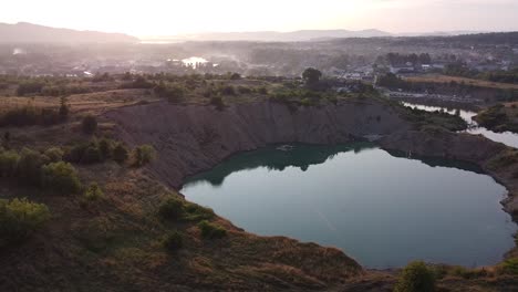 Vista-Aérea-De-Un-Lago-Minero-En-Ucrania-Al-Amanecer-Con-Niebla-Y-Casas-En-El-Fondo