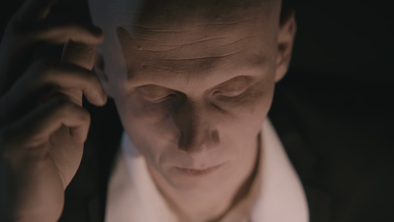 Pale bald accountant looks through the tax papers in the weird room at night