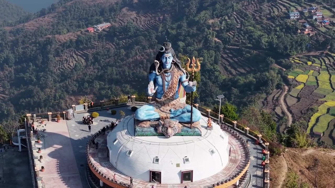Tomada aérea de drone da enorme estátua de Shiva numa crista de montanha com vista para a vasta paisagem de Pumdikot.