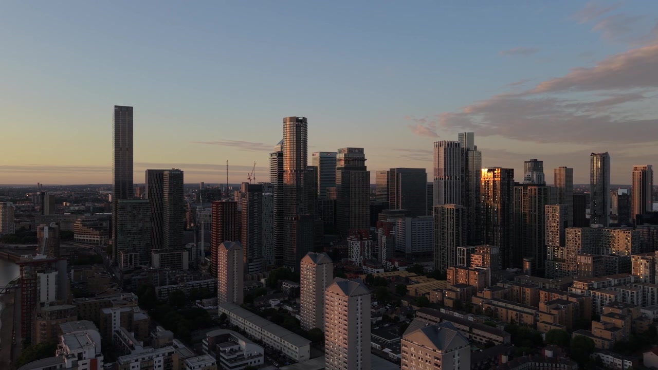 Vista panorâmica do moderno distrito de Canary Wharf em Londres ao pôr do sol. A luz solar dourada ilumina arranha-céus de vidro e edifícios residenciais.