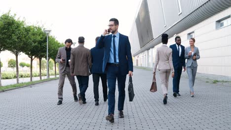 young caucasian happy businessman walking down the street and talking on the phone in the morning