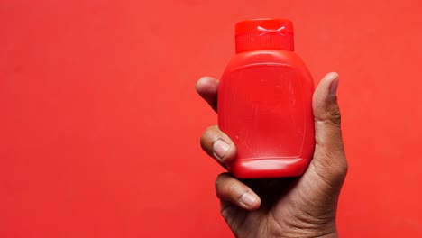 hand holding a small red sauce bottle