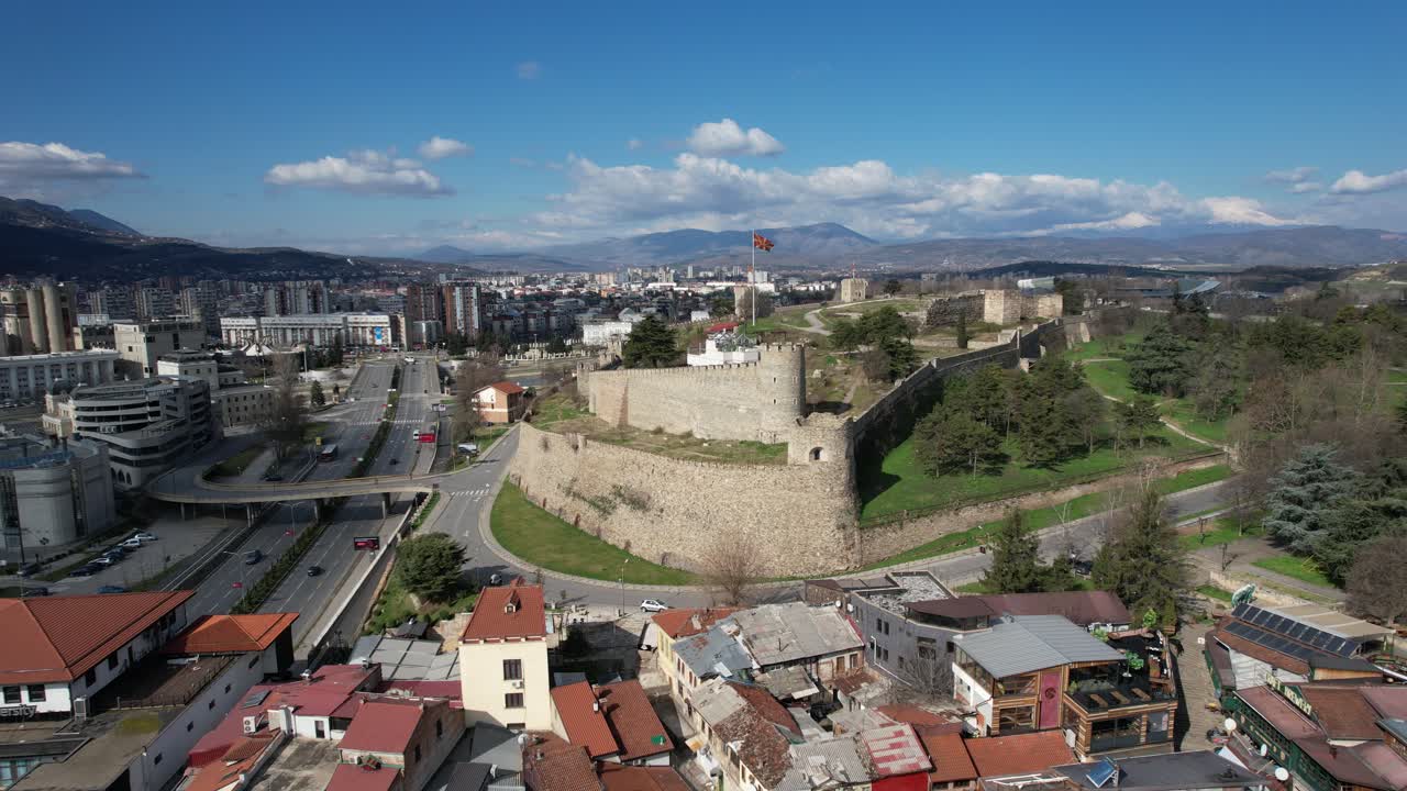 el castillo en el centro de skopje está entre los edificios, la bandera ondeando en el jardín del castillo