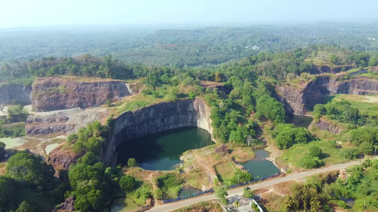 Aerial view of a rock quarry surrounded by lush greenery and deep pits with water, featuring roads and vehicles. Ideal for nature, industry