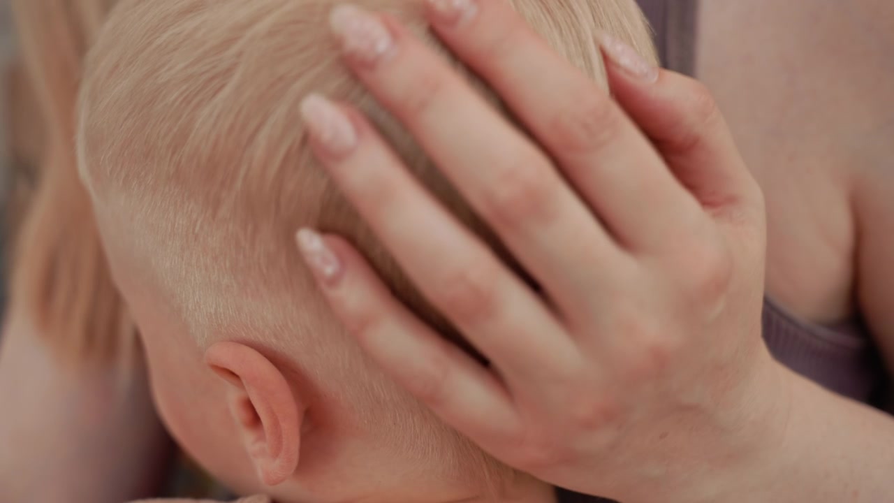 Una donna accarezza delicatamente la testa di un bambino, concentrandosi sulla tenera interazione tra madre e figlio. La vista ravvicinata evidenzia le texture morbide della pelle e i delicati movimenti della mano mentre la donna gli culla il collo.