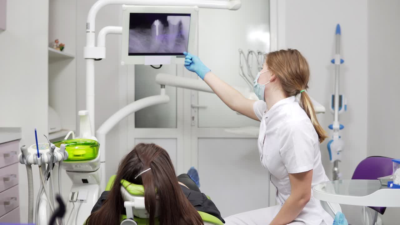una joven dentista está mostrando dientes de rayos x en una tableta en la silla. una dentista en máscara y bata de laboratorio. dientes sanos y atención dental.