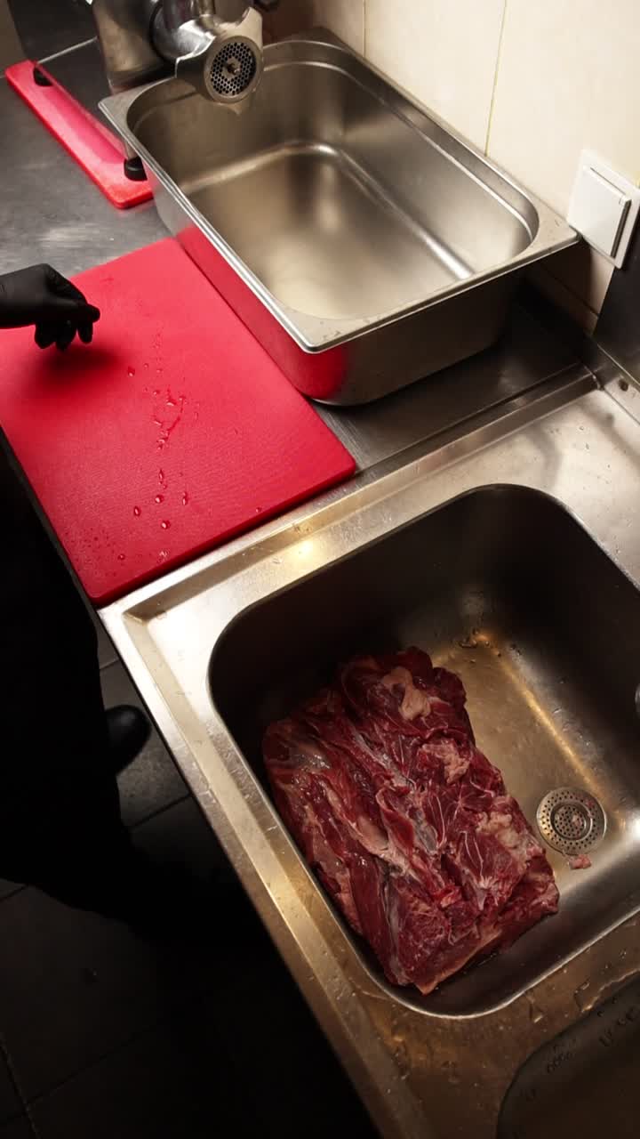 Chef in Black Gloves Handling Raw Meat in a Commercial Kitchen