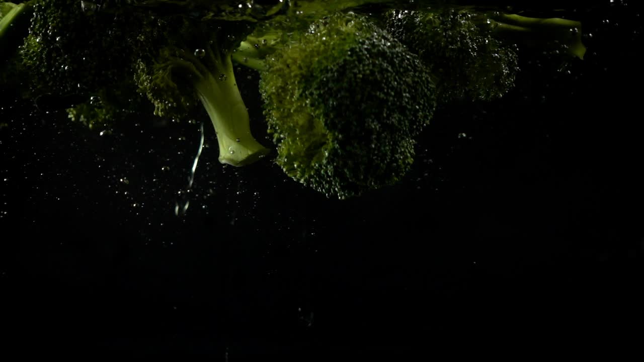Caduta di un broccolo in acqua. Slow motion. Sfondo nero.