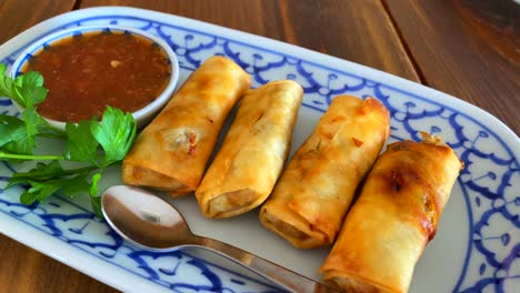 rollitos de primavera tradicionales con salsa de chili dulce en un plato blanco y azul en un restaurante tailandés, tiro en movimiento de 4k