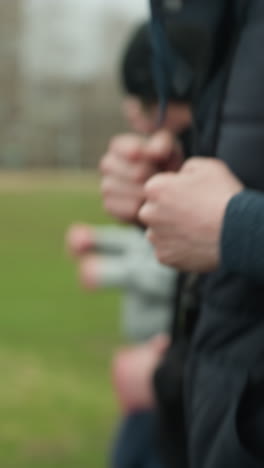 close-up of three people jogging on a track near a grassy field, with a clear view of the adult in the foreground and a blurred view of the other young boys in the background