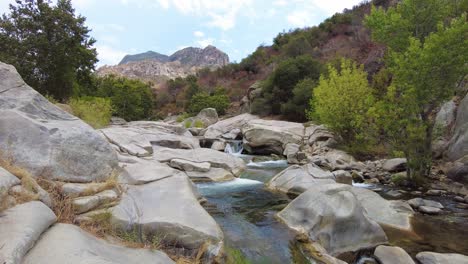 Cascadas-Sobre-Rocas-En-El-Paisaje-Forestal-Con-Montañas-Y-Cielo-Azul