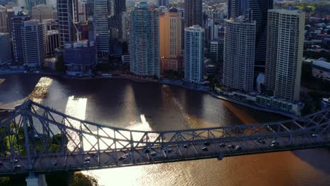 sunlight shining through high rise buildings in brisbane cbd with view of transportation at story bridge across brisbane river in australia - pullback drone