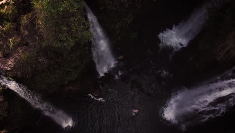 bird's eye view of a man relaxing in a big pool of water with four huge waterfalls gushing all around him