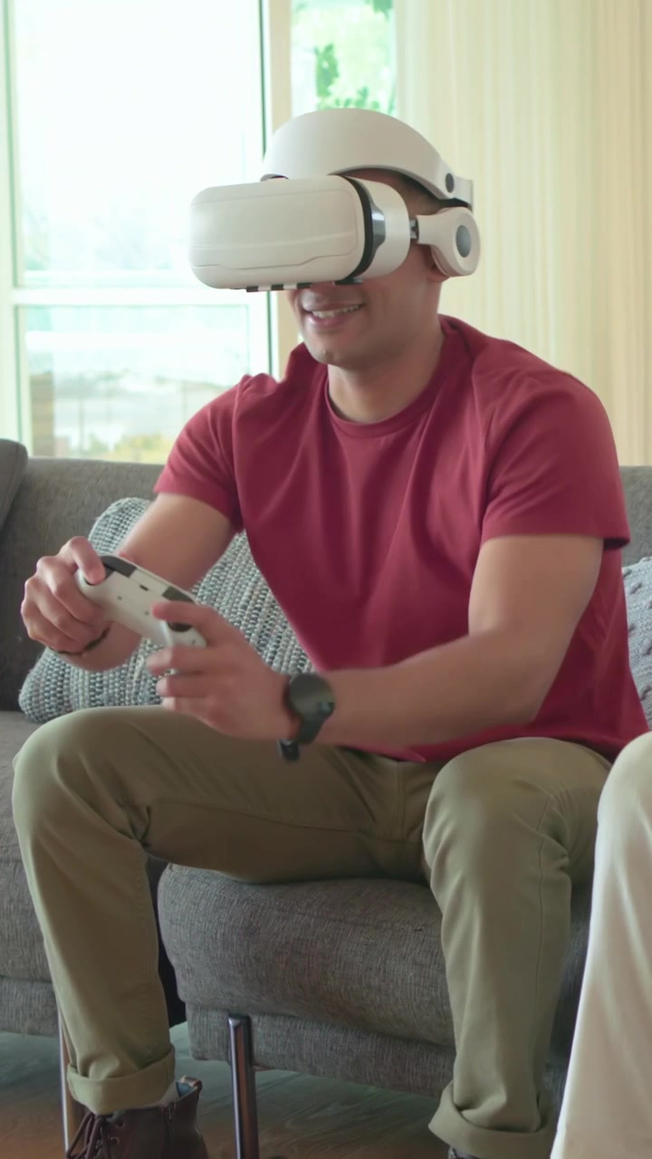 Video verticale: Reazione alla VR, un uomo con maglietta rossa indossa il visore VR e regola il controller a casa.
