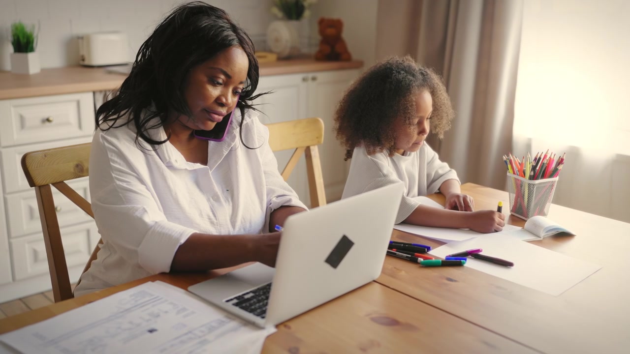 Mother Working on Laptop and Talking on Phone While Daughter Draws