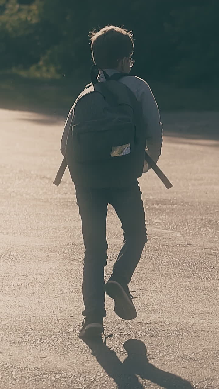 young guy with untied lacees runs along grey asphalt road holding books during schoolwork slow motion backside view