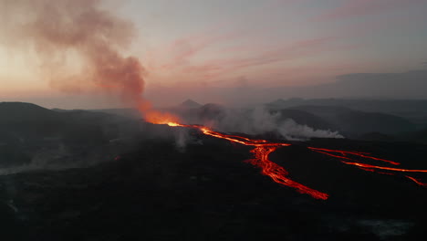 Crane-down-footage-of-erupting-volcano-against-pink-dawn-sky.-Hot-molten-lava-drawing-orange-lines-on-slope.-Fagradalsfjall-volcano.-Iceland,-2021