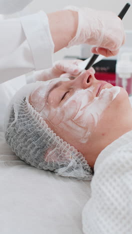 esteticista aplicando una máscara de crema hidratante química médica en el rostro de una mujer joven adulta