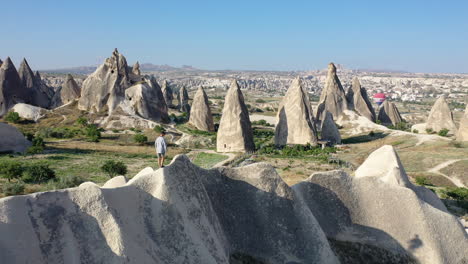 Rotating-revealing-cinematic-drone-shot-of-a-man-climbing-over-the-top-of-a-hill-in-Cappadocia,-Turkey