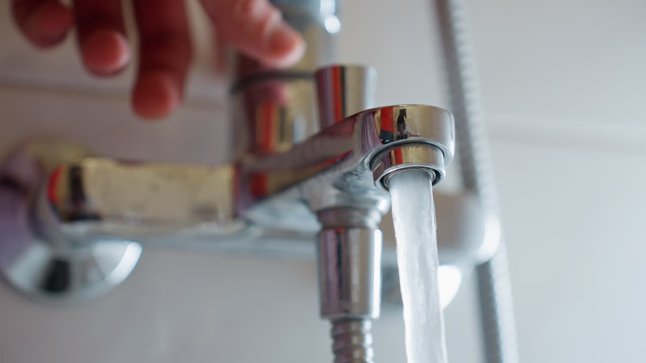 Close up of water rushing out from shiny chrome faucet tap in bathroom, blurred hand removing after turning handle, showing household plumbing, hygiene, water use and daily lifestyle in detail