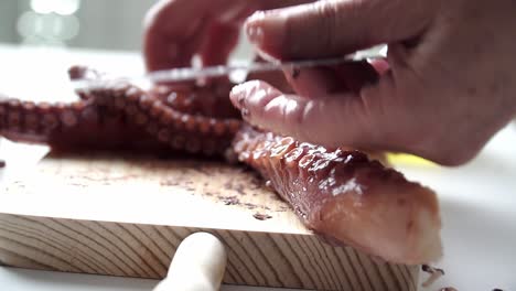 caucasian person with old hands cutting octopus tentacles and seasoning them to be cooked, on a wooden board