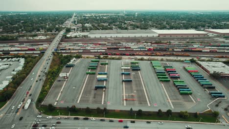gran terminal de carga junto a un complejo de carga de tren con vagones y remolques de diferentes colores junto a una carretera llena de tráfico