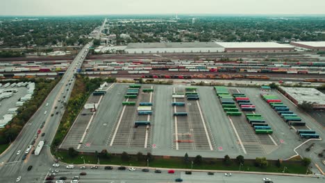 large freight terminal next to a train cargo complex with wagons and trailers of difrent colors next to a road full of traffic