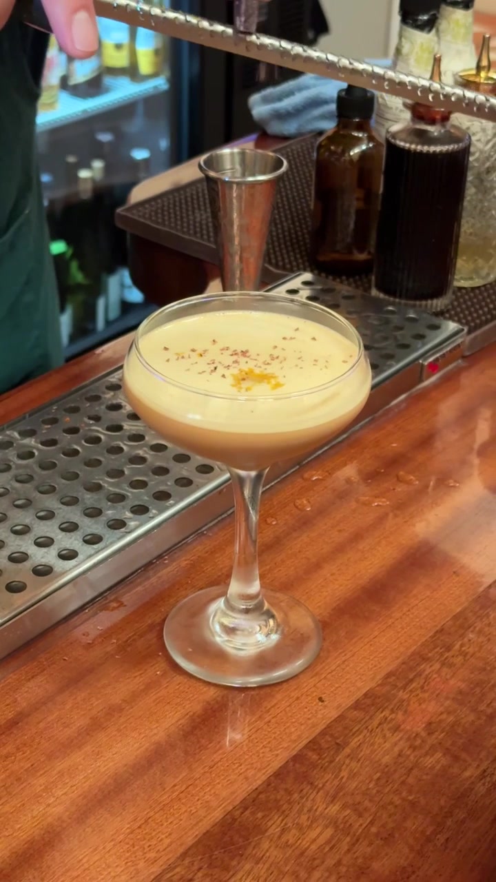 Elegante cocktail cremoso servito in una coppa con guarnizione di scorza d'arancia su un bancone da bar professionale