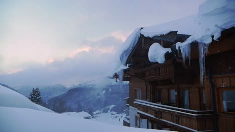 Chalet-De-Madera-Cubierto-De-Nieve-Con-Carámbanos-Y-Nieve-Arrastrada-Por-El-Viento-Durante-La-Puesta-De-Sol