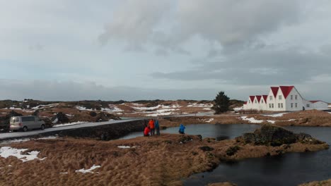 people are standing near the sea, and a white and red house is in front of them