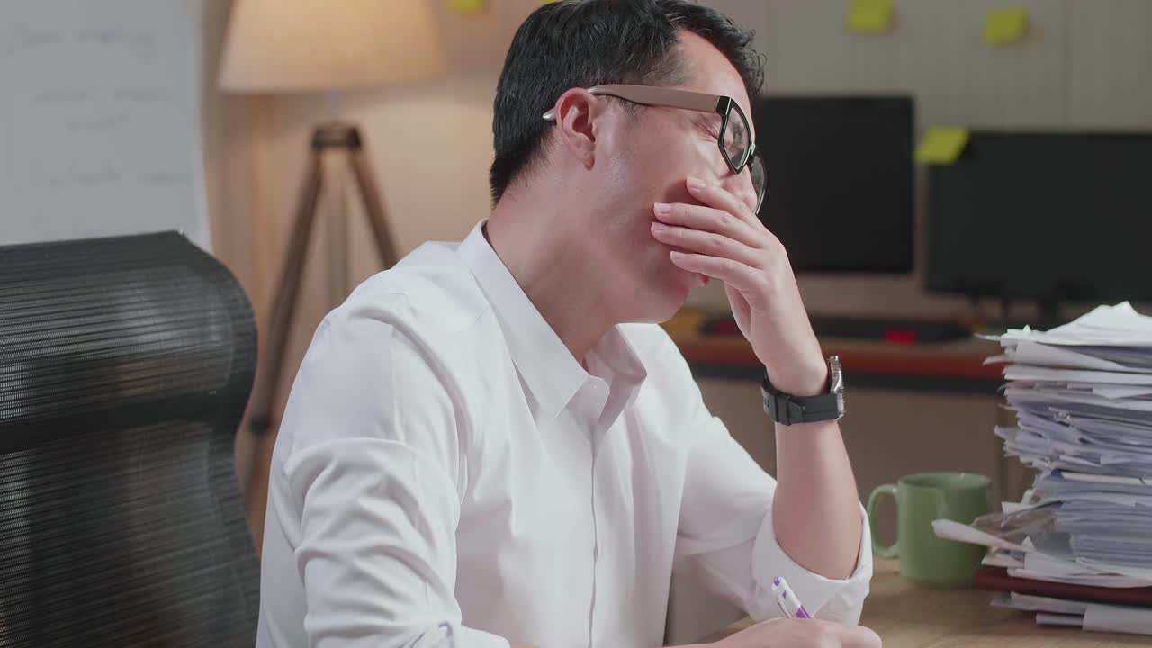 Close Up Of Tired Asian Man Yawning And Taking Off His Glasses Before Sleeping While Working Hard With Documents At The Office