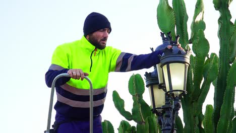 electrician in work clothes fixing a lamppost outside a villa with a cactus nearby