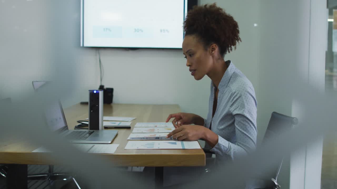 Femme d'affaires d'origine diverse assise à son bureau, vérifiant des documents et utilisant un ordinateur portable