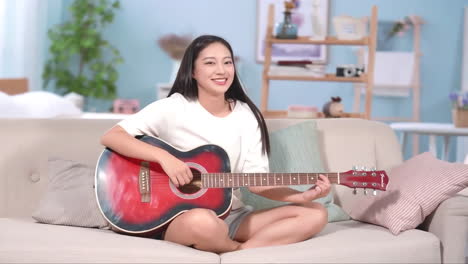 young cute girl sitting cross-legged on the sofa enjoyed playing guitar