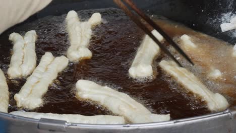 cook prepare youtiao, also known as chinese fried churros, chinese cruller, chinese oil stick, chinese doughnut, you char kway, cakwe, cakoi, kueh, kuay and fried breadstick. street food concept. closeup. 4k