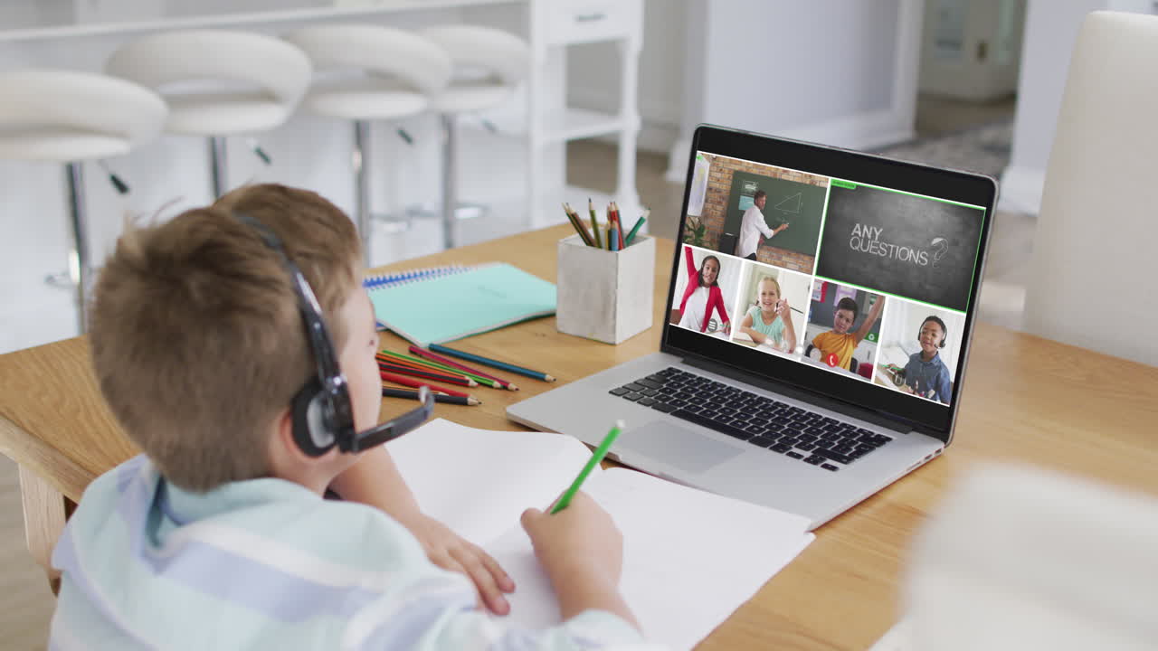 Schoolboy using laptop for online lesson at home, with diverse teacher and class on screen