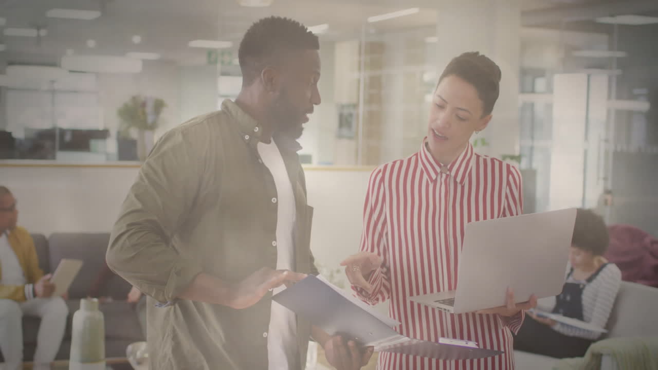 Discussing documents and laptop work, two colleagues in modern office setting