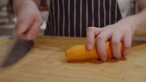 el chef corta la zanahoria en trozos en una tabla cortada de madera