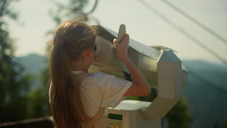 focused girl explores area popular for tourists through enormous binoculars. inquisitive child immersed in discovering spectacular mountainous terrain