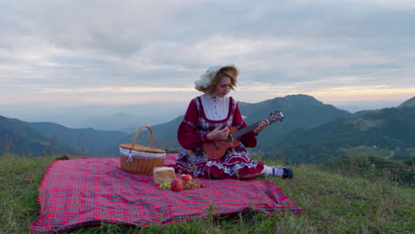 Ropa-Tradicional-Medieval-Renacentista-Modelo-Femenino-Tocando-El-Ukelele-Mientras-Come-En-La-Naturaleza