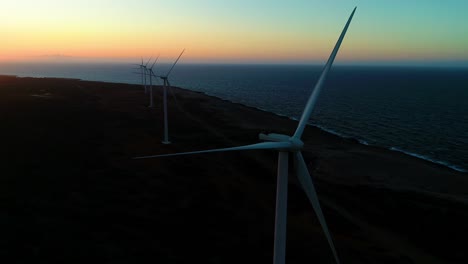 Windturbinenlinie-In-Der-Dämmerung-Der-Blauen-Stunde-Am-Meeresufer,-Sonnenuntergang-In-Der-Goldenen-Stunde,-Luftdrohnenumlaufbahn