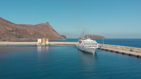 Aerial-shot-over-Passenger-boat-leaving-marina-with-island-cliffs-as-background