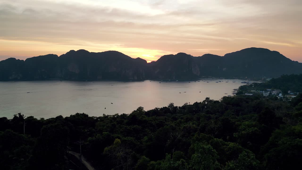 Scenic sunset over Ko Phi Phi Don, Thailand, with dramatic cliffs, calm bay, boats, and lush jungle foreground