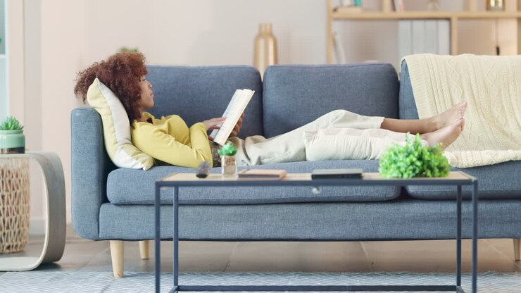 Relaxed black woman reading a funny book on a sofa
