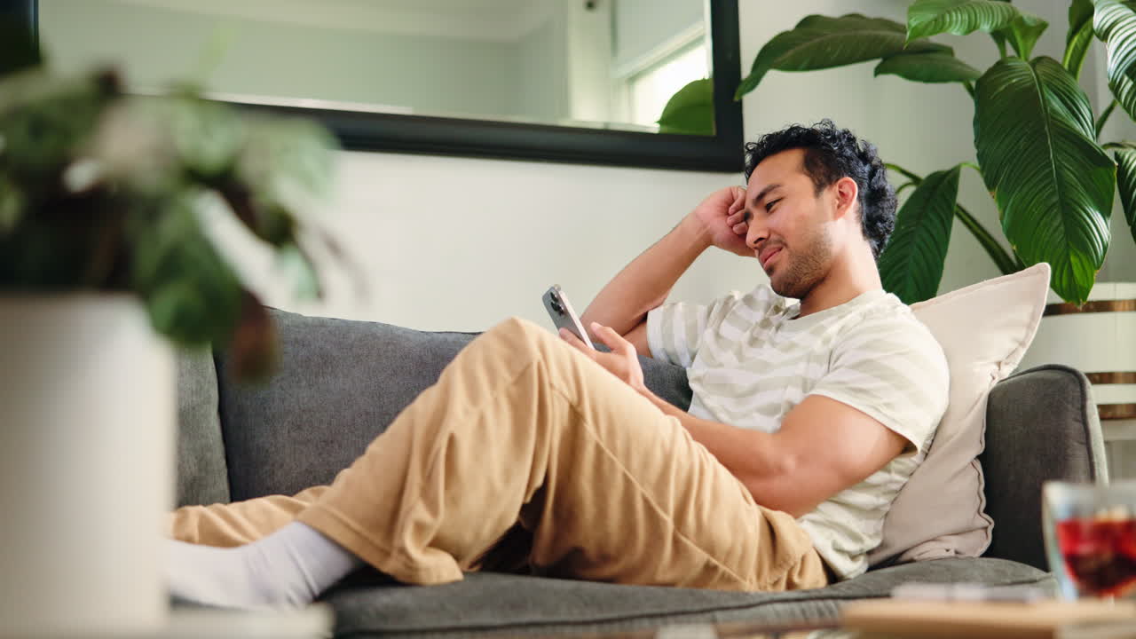 Giovane uomo che si rilassa sul divano e usa lo smartphone a casa.