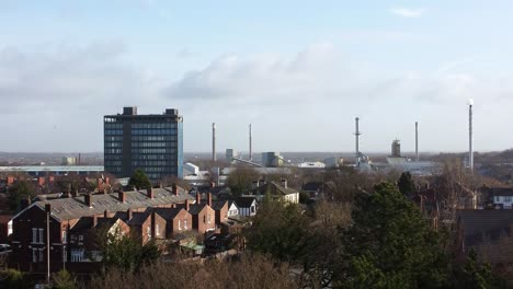 Aerial-view-over-park-trees-to-industrial-townscape-housing-with-blue-skyscraper,-Merseyside,-England