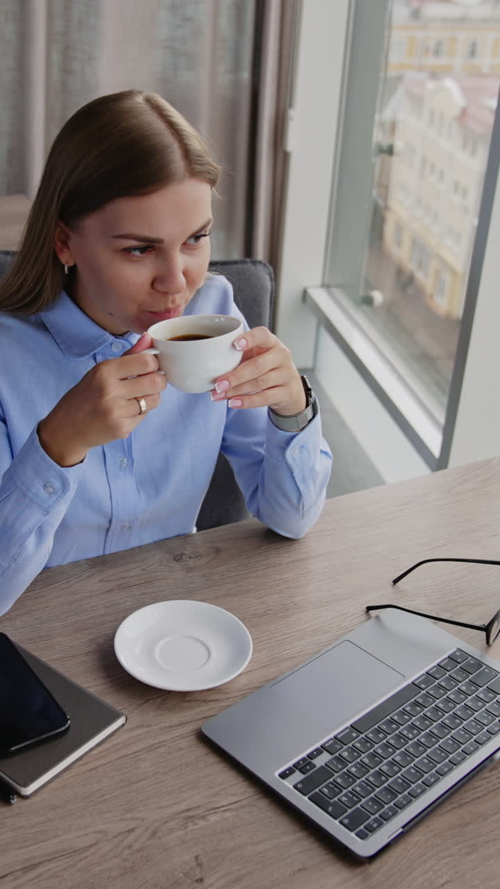 Kvinde drikker kaffe ved sit skrivebord på en café med udsigt over byen